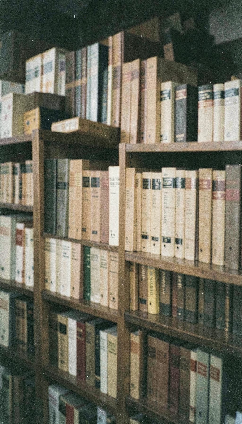 Una fotografía analógica con grano visible de una biblioteca técnica con volúmenes encuadernados en tonos beige y marrón, estantería de madera, atmósfera serena y estudiosa.